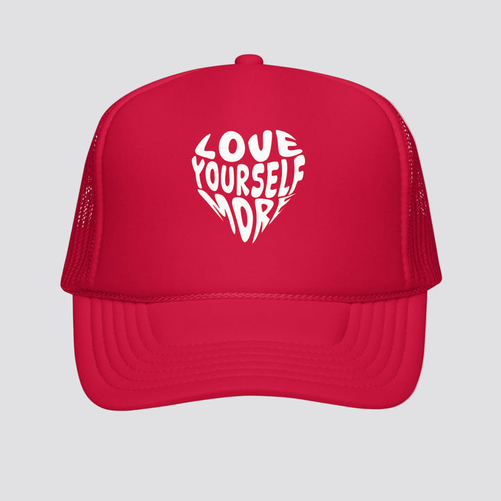 Red cap with 'Love Yourself More' text in a heart shape on a white background