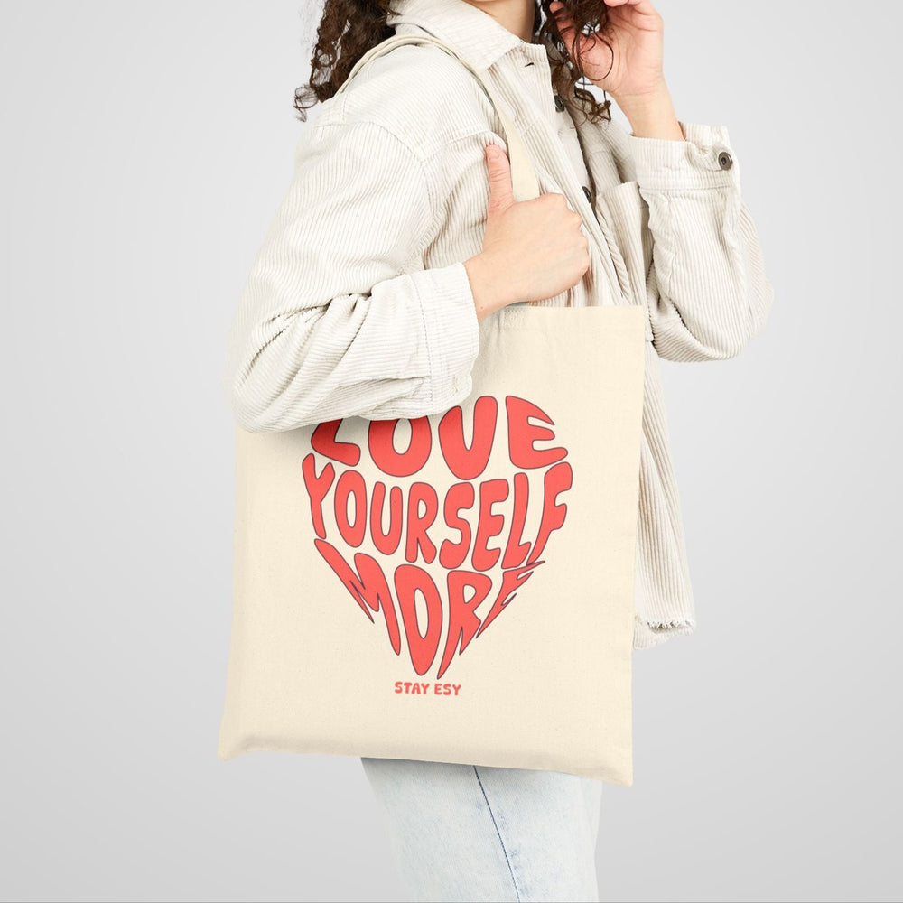 Woman holding a tote bag with 'Love Yourself' design on a plain background