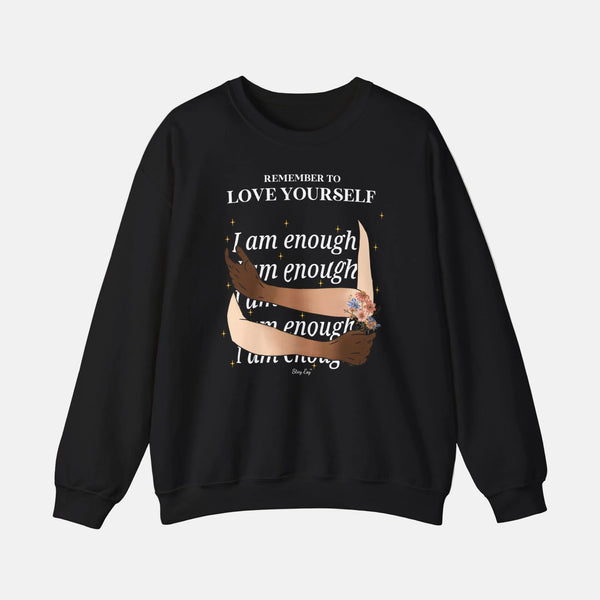 A black crewneck sweatshirt with a graphic print on the front. The design features the text 'REMEMBER TO LOVE YOURSELF' in white, followed by 'I am enough' repeated in white script overlaid with a brown ribbon illustration and small colorful floral accents.