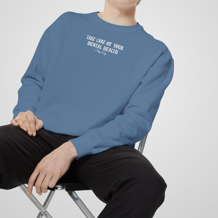 Person wearing a blue sweatshirt with text, sitting on a chair against a plain background