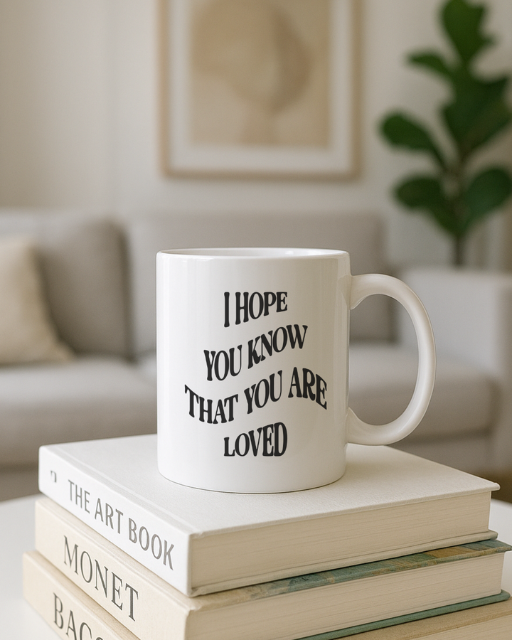 White mug with motivational quote on a stack of books in a cozy living room.
