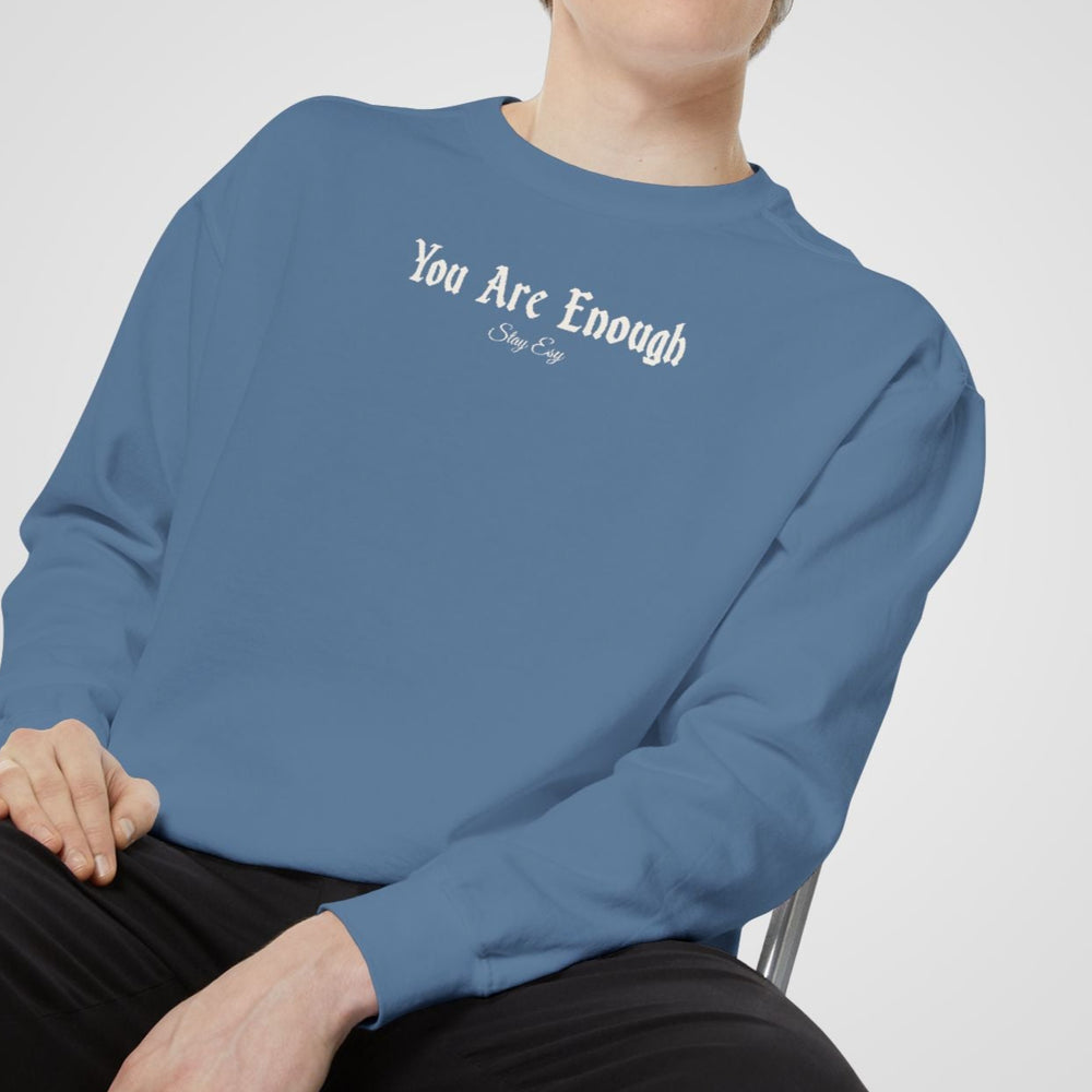 Person wearing a blue sweatshirt with text, sitting on a chair against a plain background