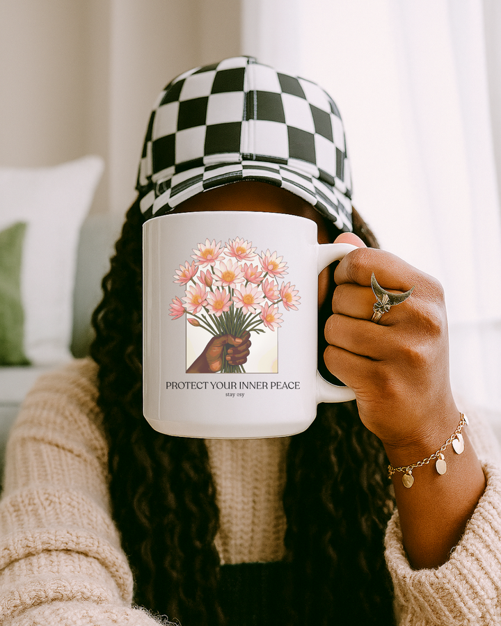 Person holding a mug with a floral design and text, wearing a checkered hat and beige sweater.