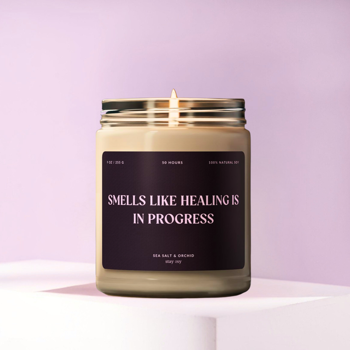 Candle with a label 'Smells like healing is in progress' on a light purple background