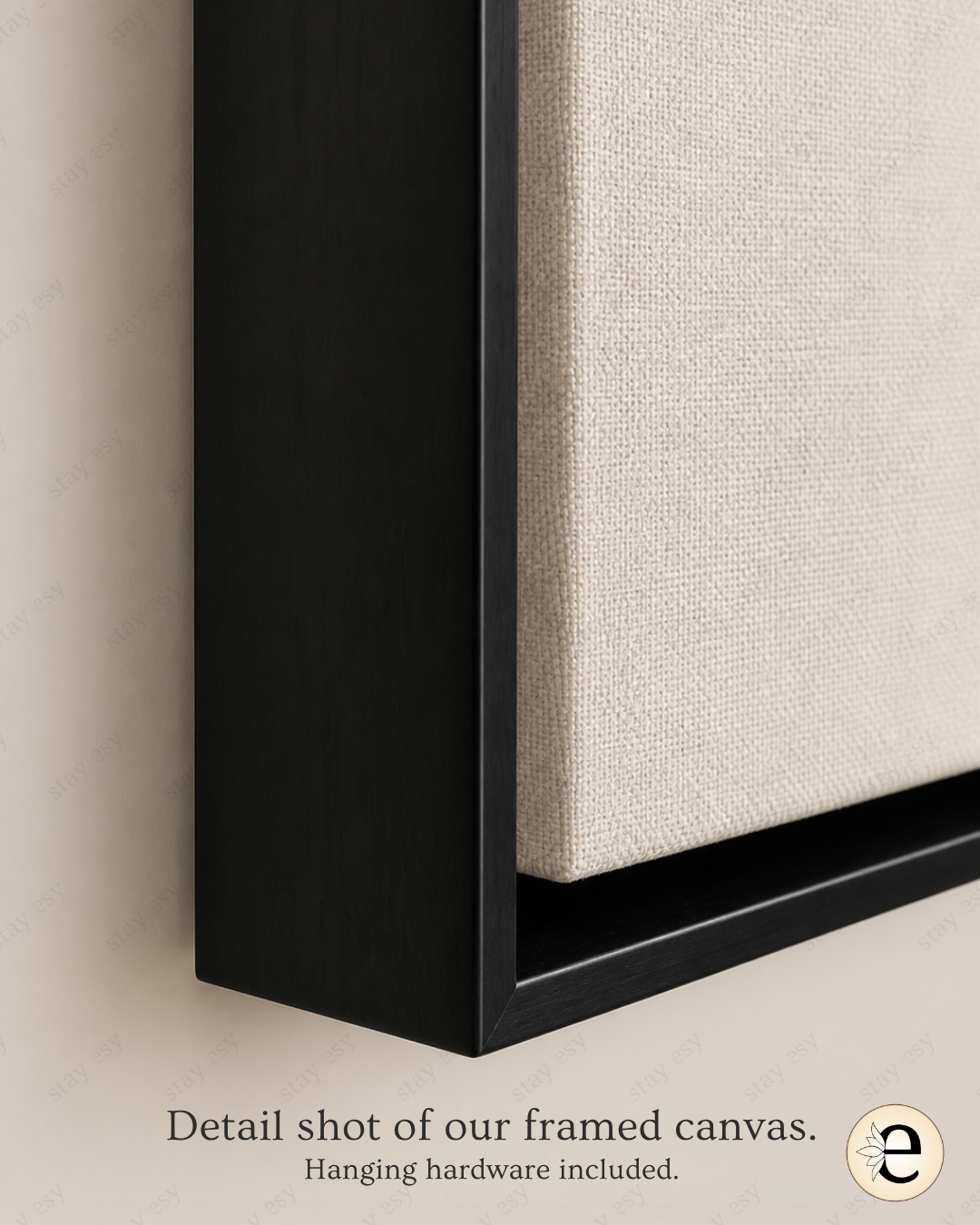 Close-up detail shot of a framed canvas wall art piece, showing a black frame and textured off-white fabric panel against a beige wall, with text reading &