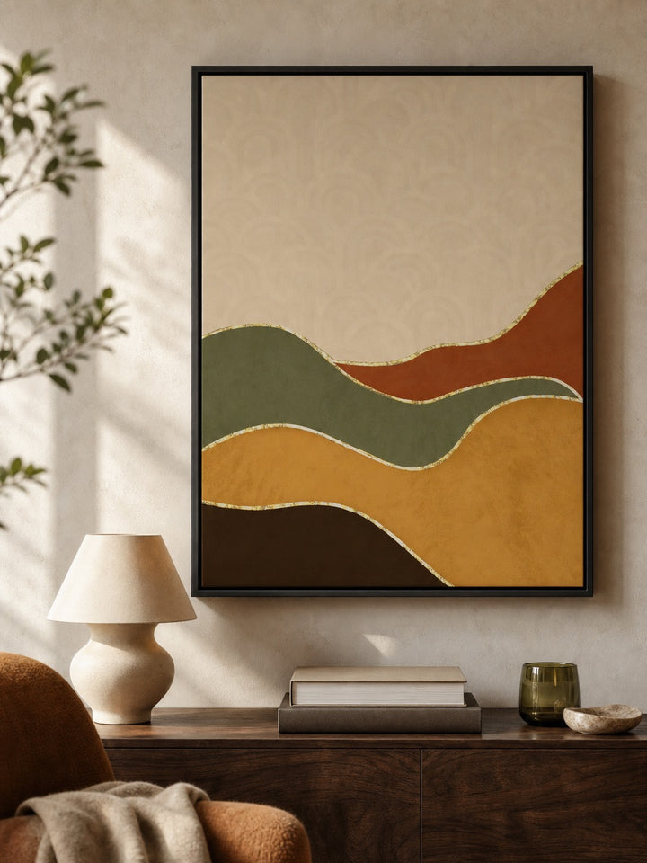 A framed abstract wall art print hangs on a beige wall above a wooden console table. The artwork features flowing, wavy shapes in muted mustard yellow, olive green, terracotta orange, dark brown, and cream, outlined with thin gold-like lines.
