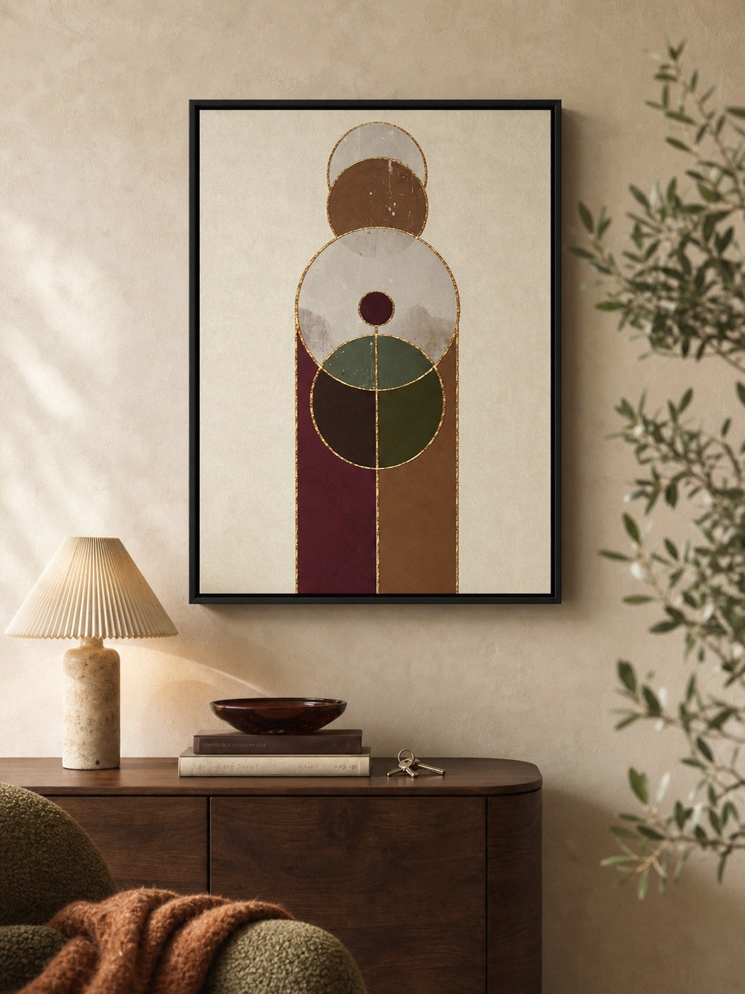 Framed abstract geometric wall art hanging on a beige wall above a dark wood console table, with a lamp, books, and a plant visible in the room.