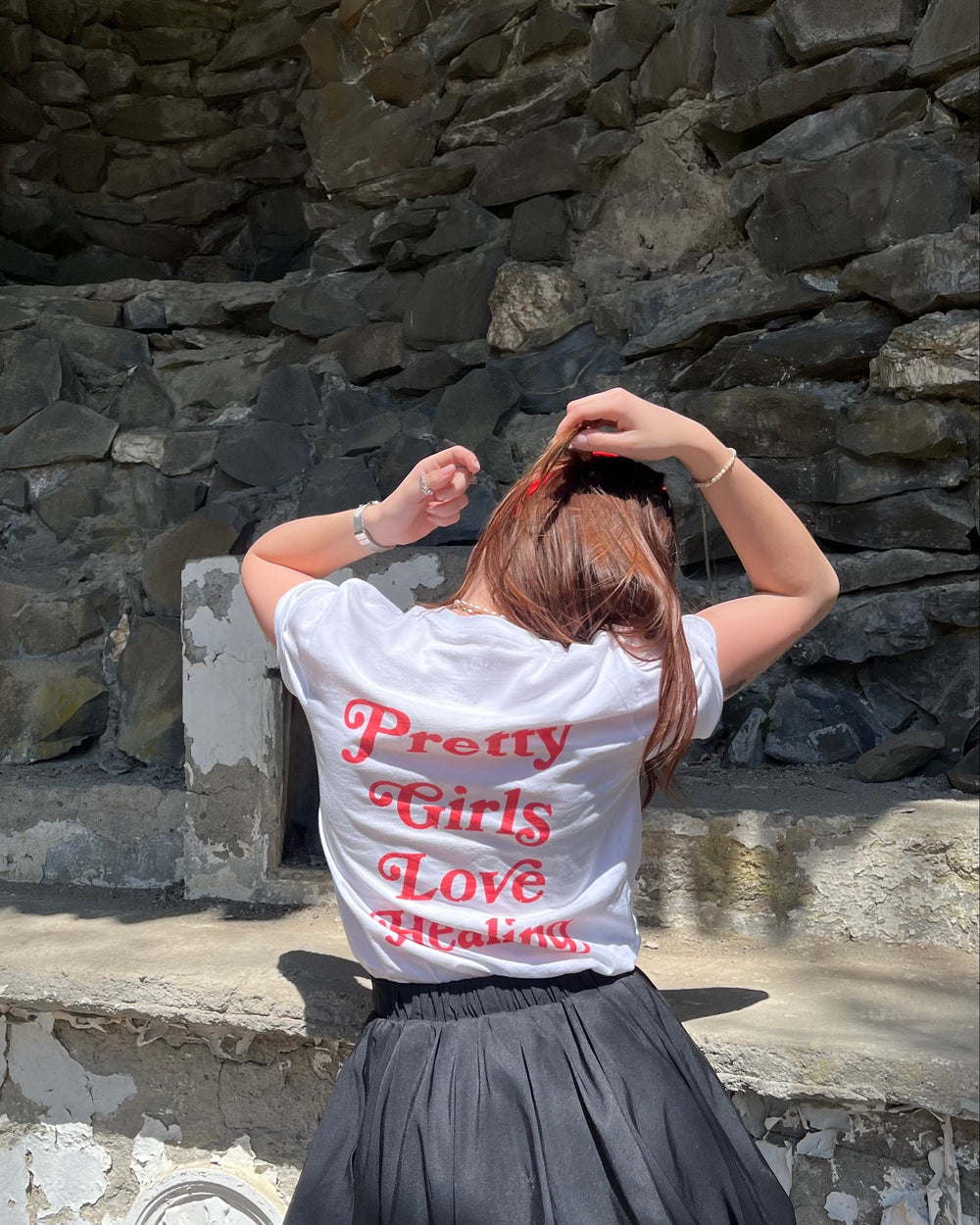 Person wearing a white shirt with red text sitting against a stone wall.