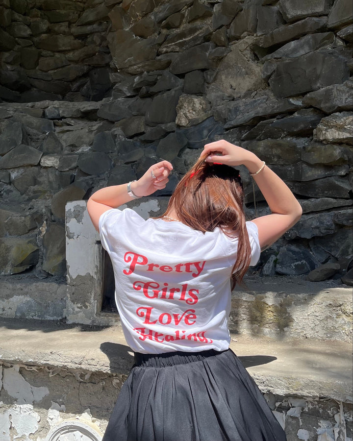 Person wearing a white shirt with red text sitting against a stone wall.