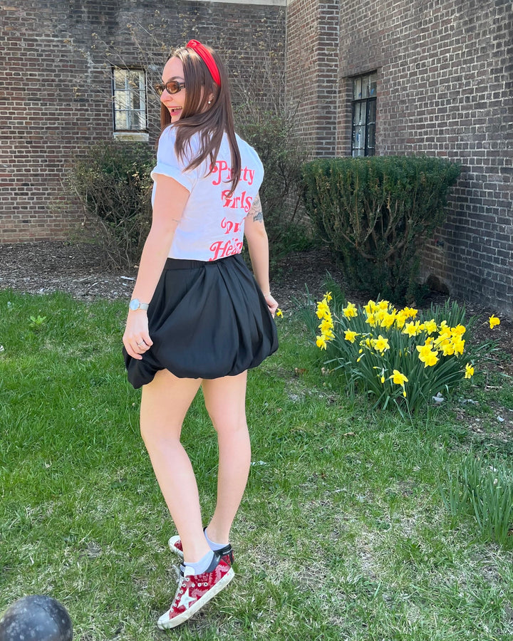 Person standing in front of a brick building with flowers and greenery