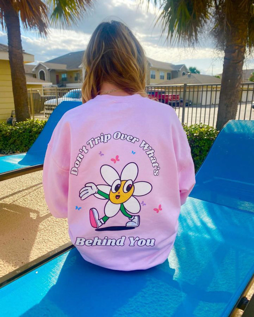 Person wearing a pink sweatshirt with a cartoon character and text on the back, sitting on a blue chair outdoors.