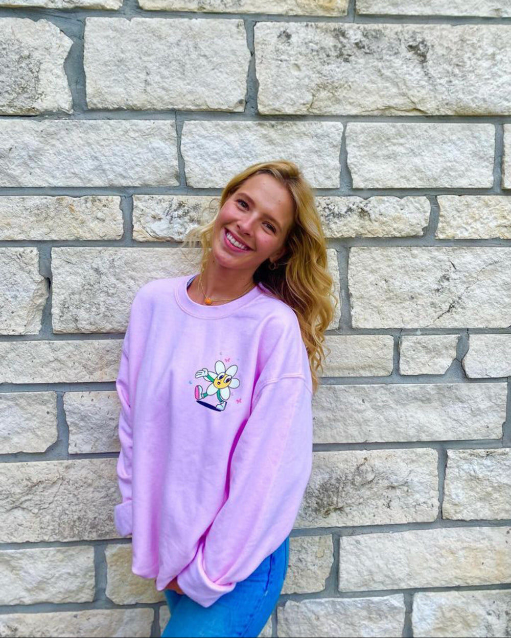 Woman wearing a pink sweatshirt with a design in front of a stone wall