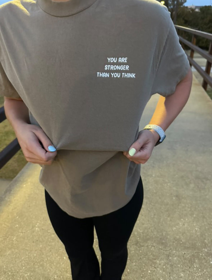 Person wearing a beige t-shirt with motivational text outdoors