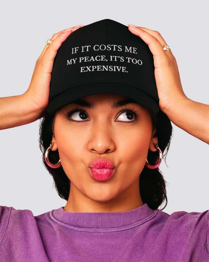 Person wearing a black cap with text and a purple shirt on a gray background