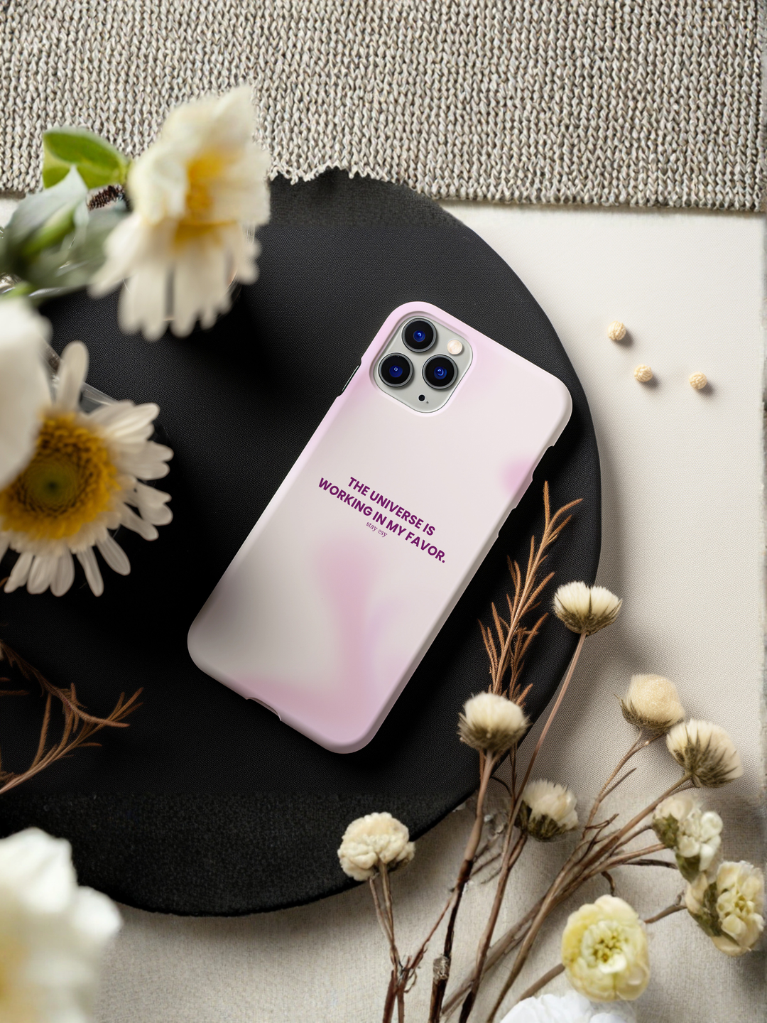 Pink phone case with text on a black plate surrounded by flowers