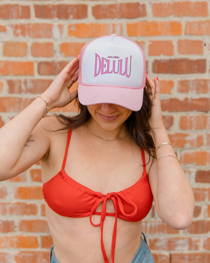Person wearing a red bikini and pink cap with 'DELU LU' text against a brick wall.
