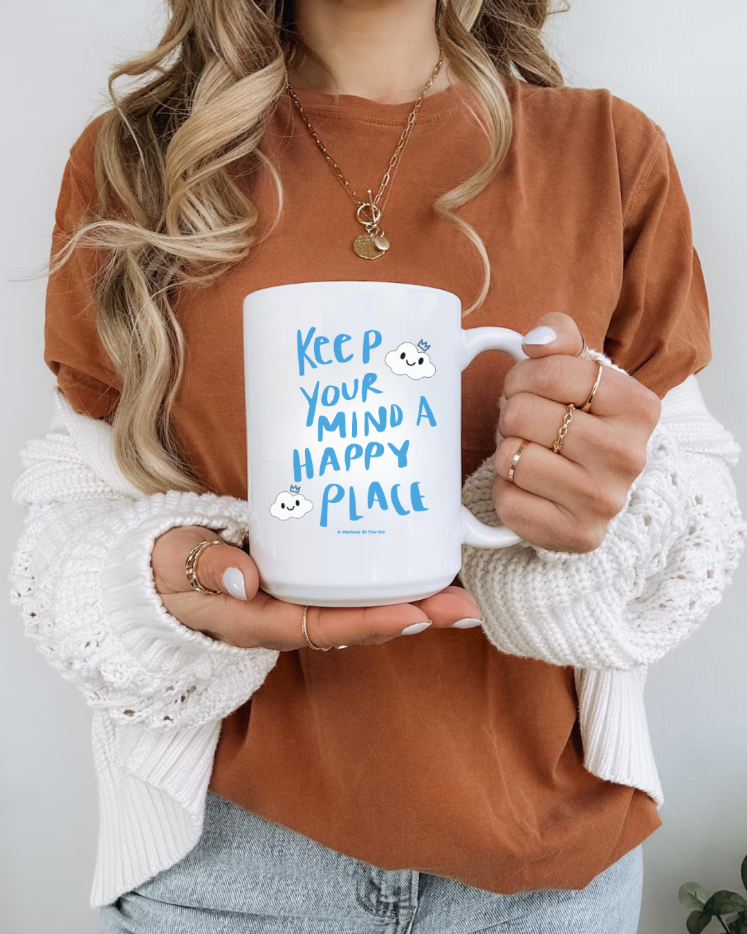 Person holding a white mug with blue text 'Keep your mind in a happy place' against a neutral background