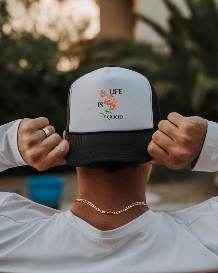 Person wearing a 'Life is Good' cap with hands holding it, blurred background