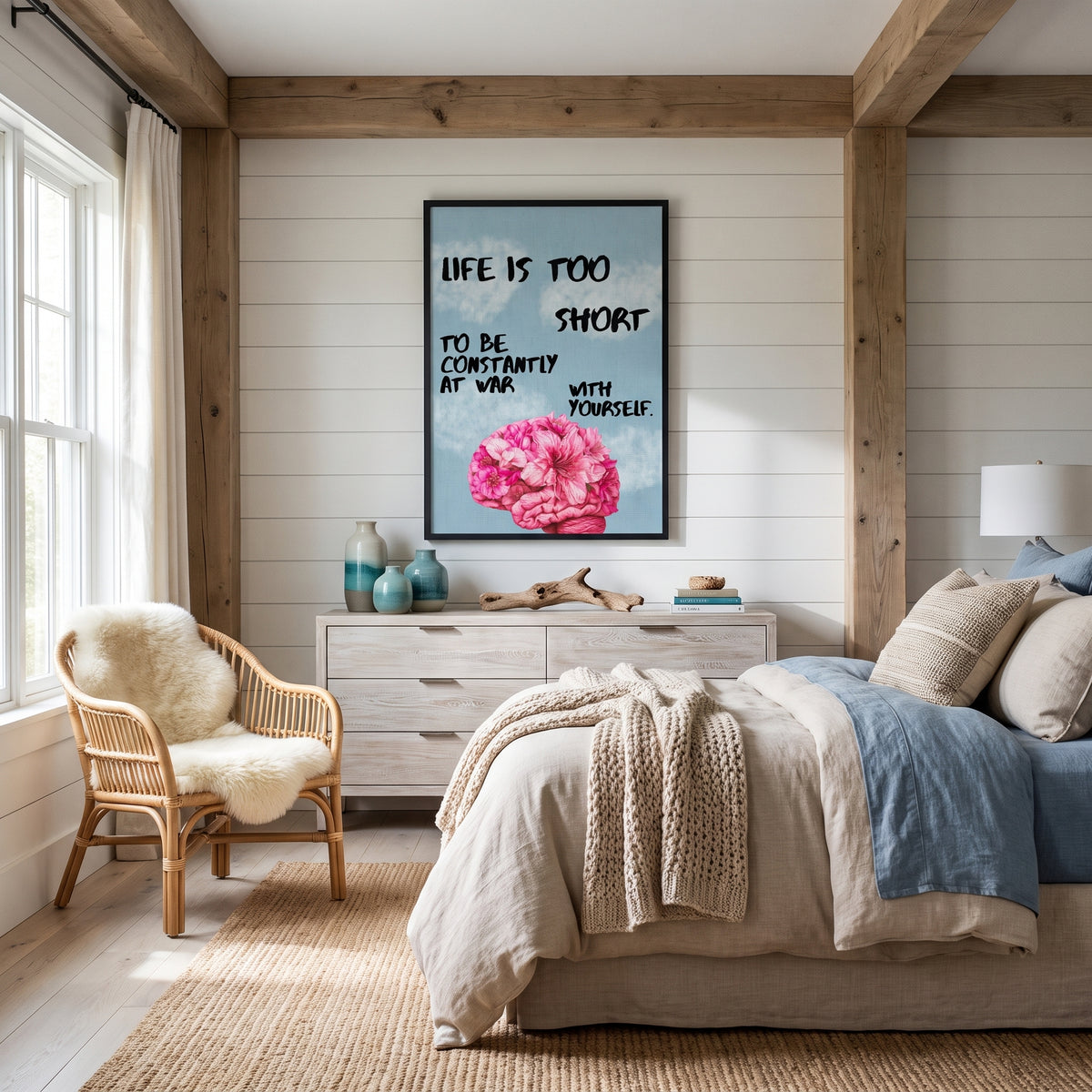 A framed wall art print featuring a pink flower and the quote 'LIFE IS TOO SHORT TO BE CONSTANTLY AT WAR WITH YOURSELF' displayed in a rustic bedroom setting with a bed, rattan chair, and wooden beams.