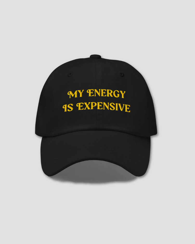 Black cap with yellow text 'MY ENERGY IS EXPENSIVE' on a light gray background