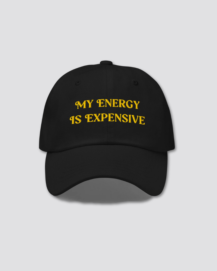 Black cap with yellow text 'MY ENERGY IS EXPENSIVE' on a light gray background