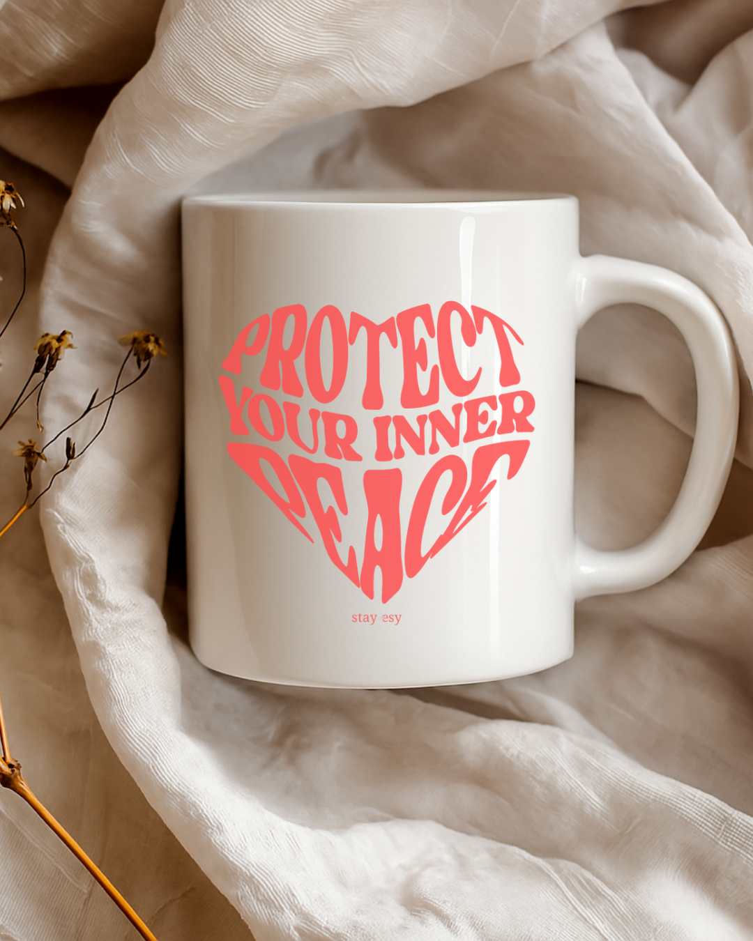 White mug with red text 'PROTECT YOUR INNER PEACE' on a beige fabric background
