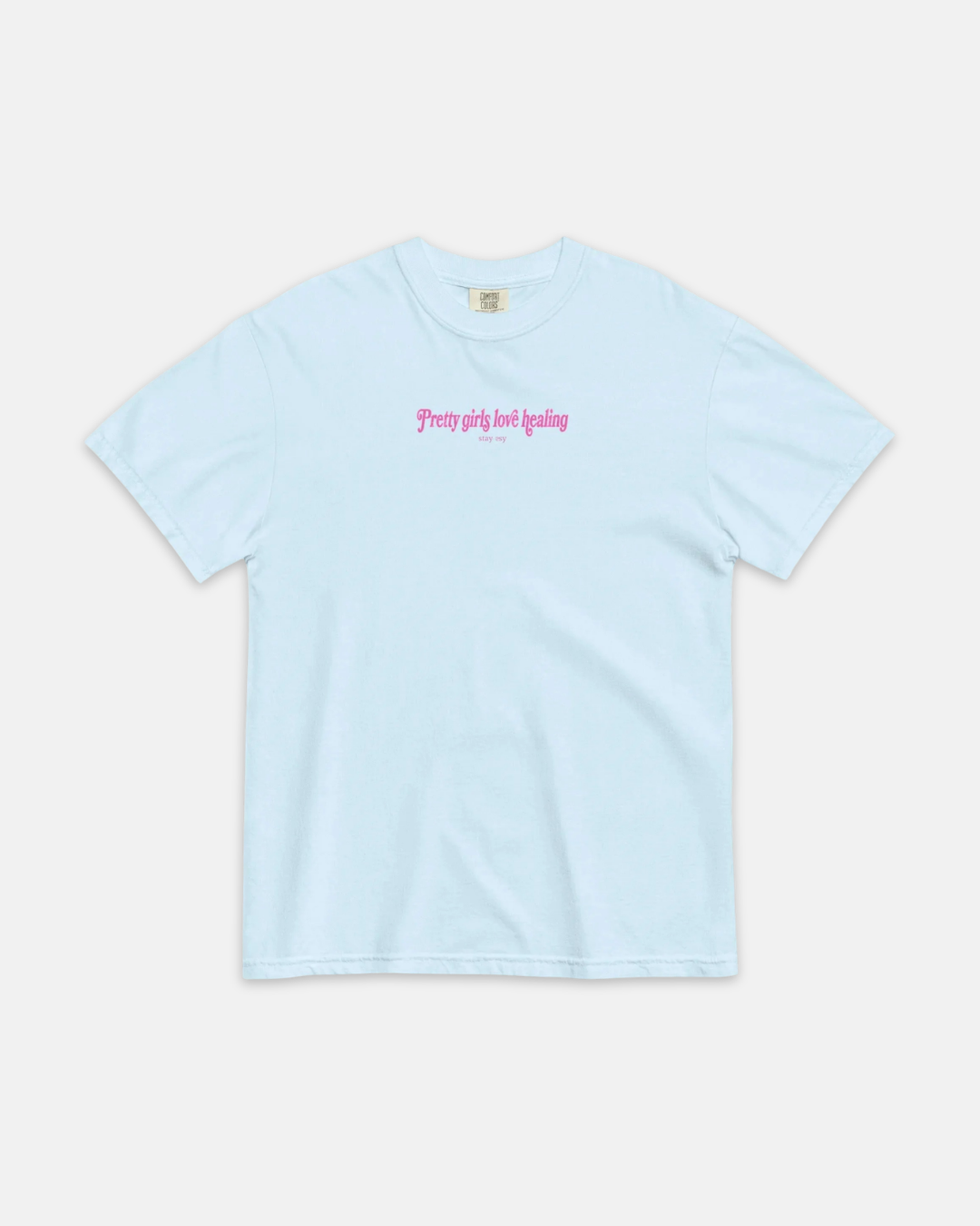 A light blue short-sleeve crewneck t-shirt with pink gothic-style text on the chest reading 'pretty girls just healing' and smaller text below, displayed flat against a light gray background.