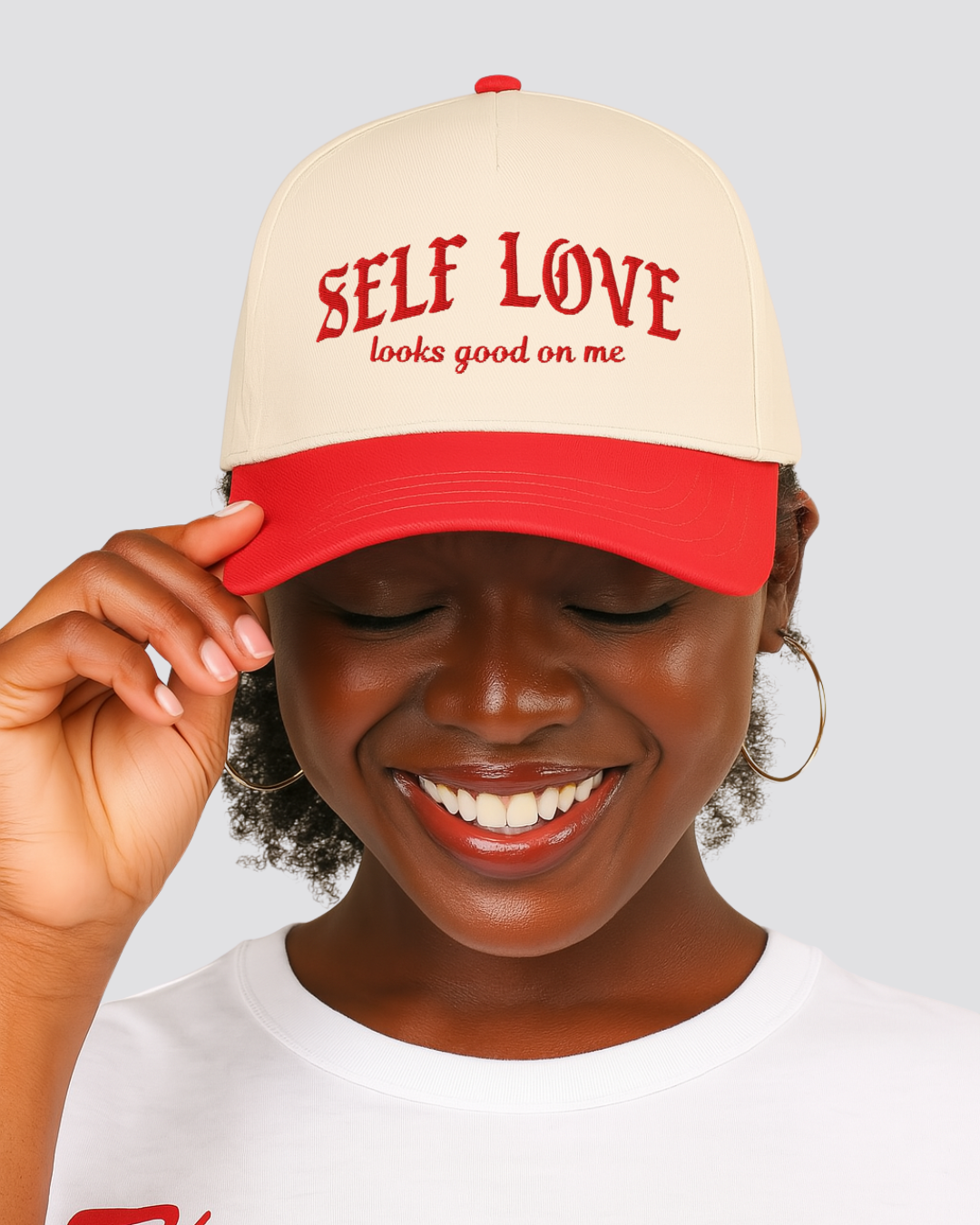 Person wearing a cap with 'SELF LOVE looks good on me' text on a light gray background