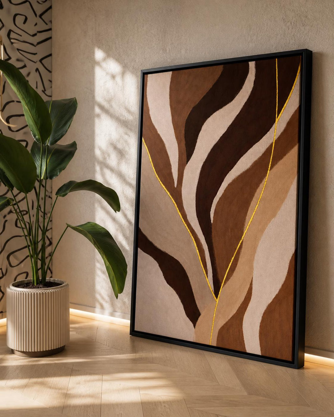 A framed abstract wall art print with flowing organic shapes in beige, brown, and cream, accented by thin yellow lines, leaning against a wall in a sunlit room next to a potted plant.