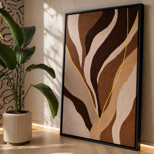 A framed abstract wall art print with flowing organic shapes in beige, brown, and cream, accented by thin yellow lines, leaning against a wall in a sunlit room next to a potted plant.