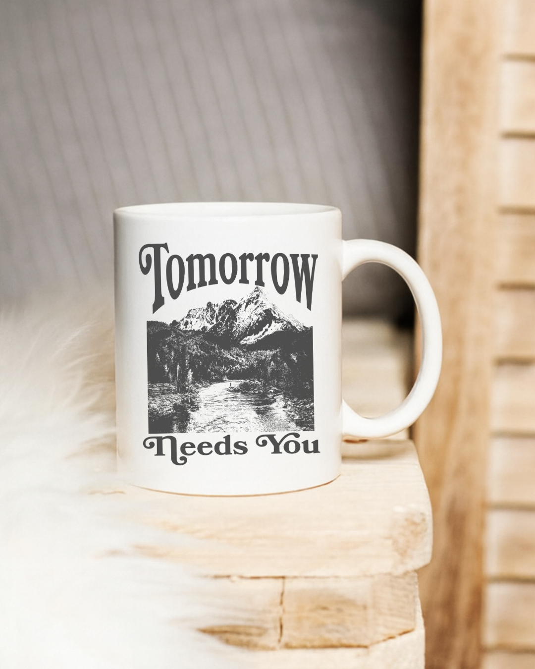 White mug with black text and mountain design on a wooden surface