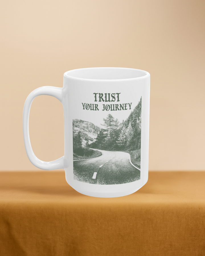 White mug with scenic design and 'Trust Your Journey' text on a beige background