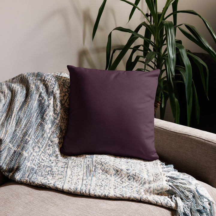 Purple pillow on a couch with a textured blanket and plant in the background