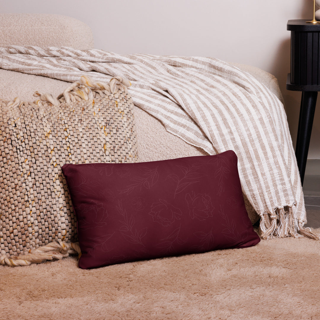 Maroon pillow with floral pattern on a beige couch with a striped blanket