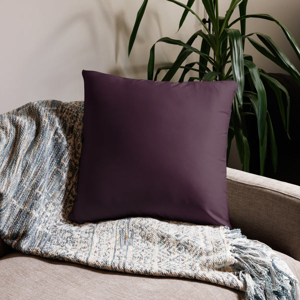 Purple pillow on a couch with a textured blanket and plant in the background
