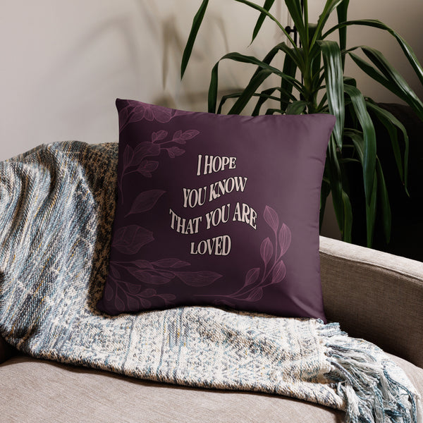 Purple pillow with motivational quote on a couch with a plant in the background