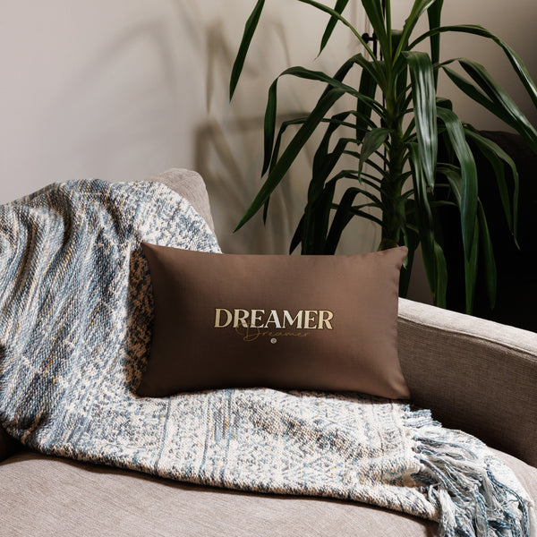 Brown pillow with 'DREAMER' text on a couch with a blanket and plant in the background