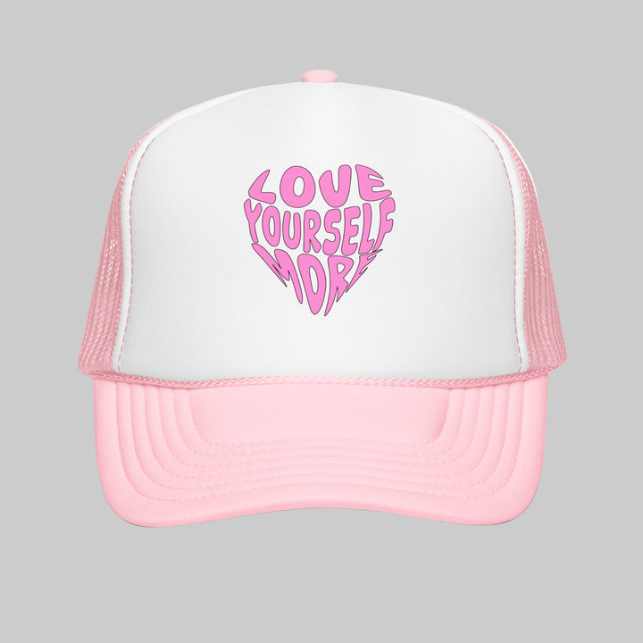 Pink and white trucker hat with 'Love Yourself More' text on a white background