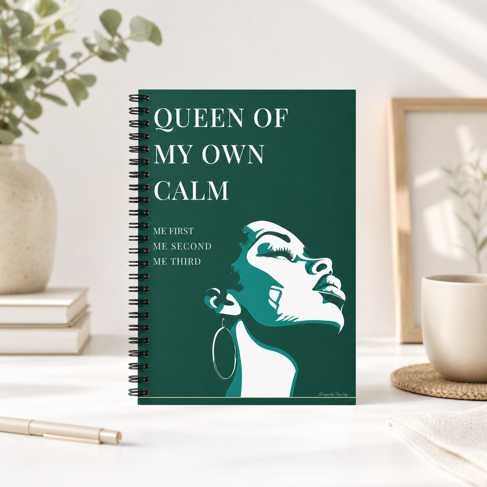 Notebook with 'Queen of My Own Calm' design on a desk with decor items.