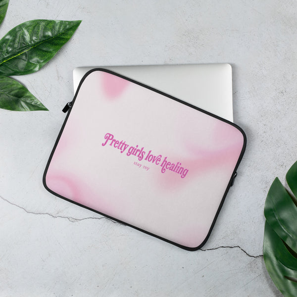 Pink gradient laptop sleeve with text on a light gray surface with green leaves.