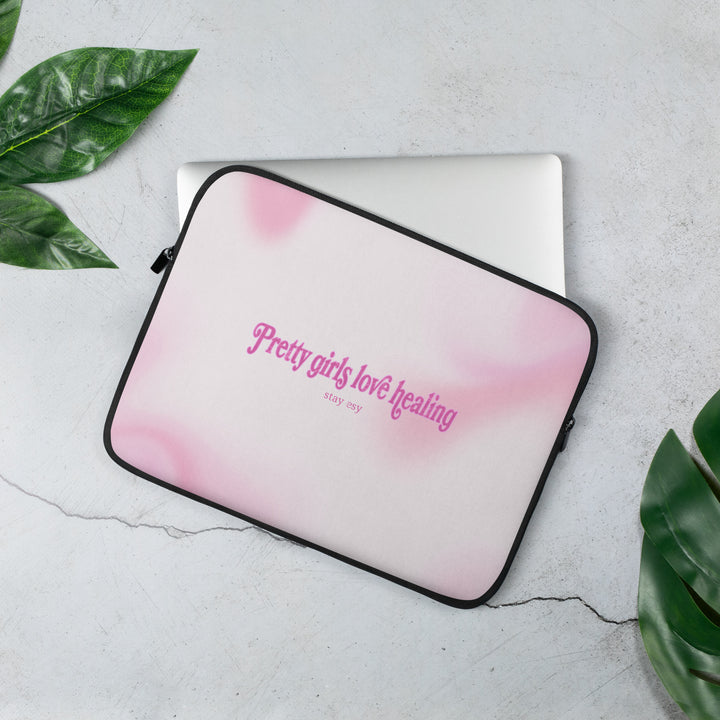 Pink gradient laptop sleeve with text on a light gray surface with green leaves.