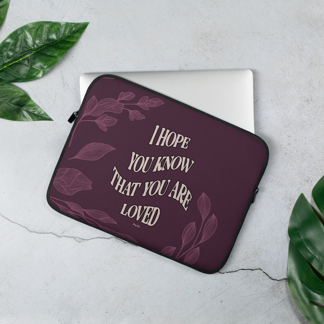 Maroon laptop sleeve with motivational quote on a light gray surface with green leaves.