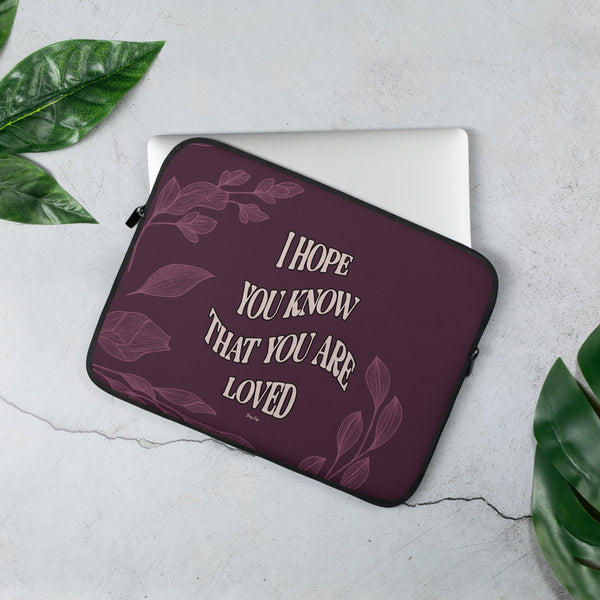 Maroon laptop sleeve with motivational quote on a light gray surface with green leaves.