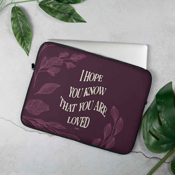 Laptop sleeve with motivational quote on a light gray background with green leaves.