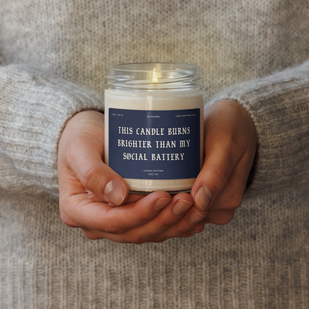 Candle held in hands with a humorous label, against a neutral background