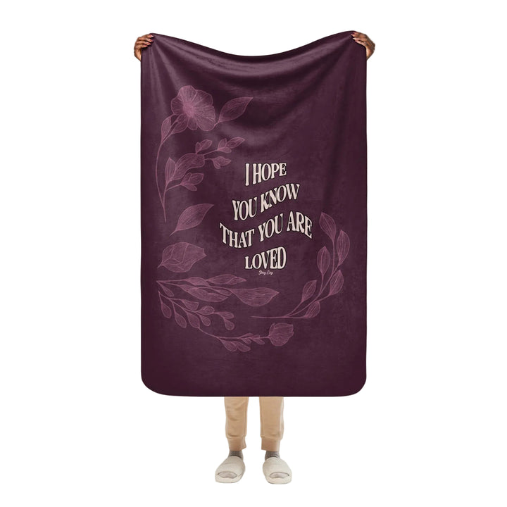 Person holding a purple blanket with floral design and text on a white background