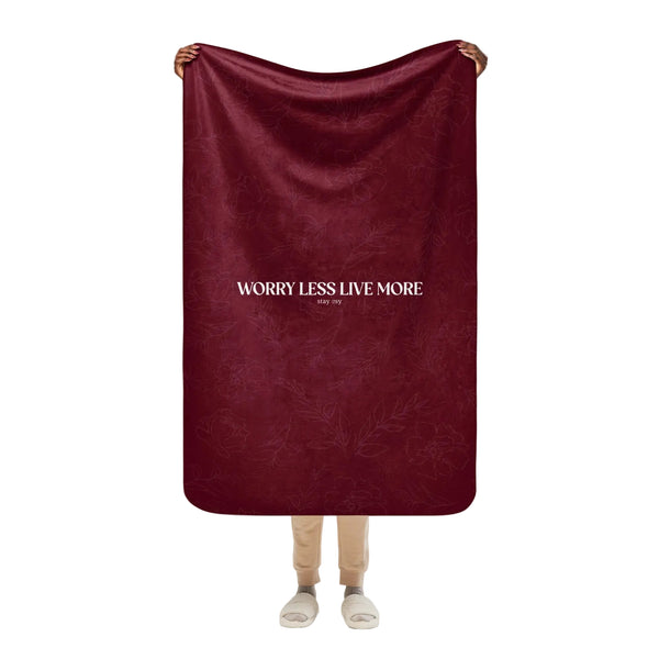 Person holding a maroon blanket with 'Worry Less Live More' text on a white background