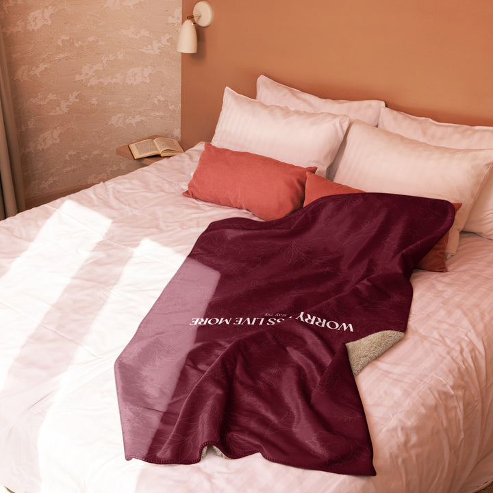 Maroon blanket with text draped over a bed with white and red pillows.