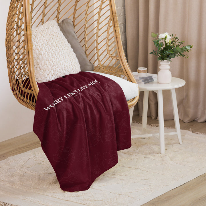 Maroon blanket with text draped over a wicker chair in a cozy room.