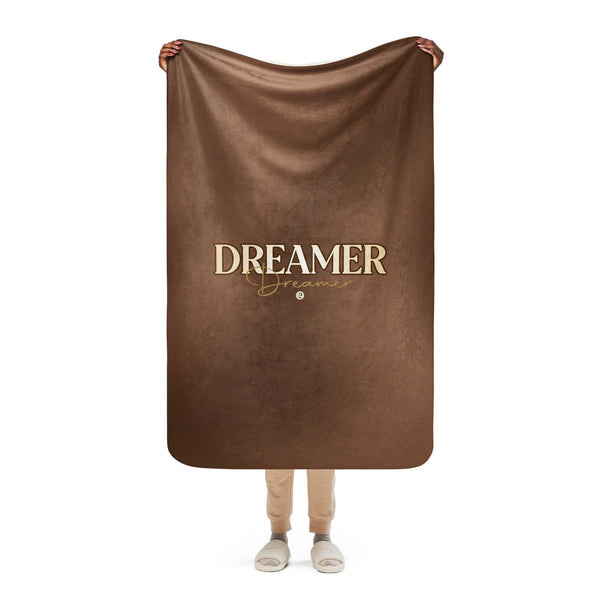 Brown blanket with 'DREAMER' text held by a person on a white background